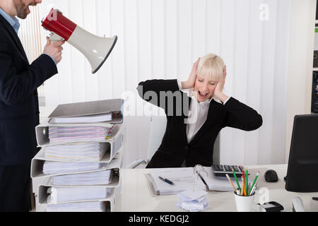 Boss Shouting At Young Businesswoman Through Loudspeaker In Office Stock Photo