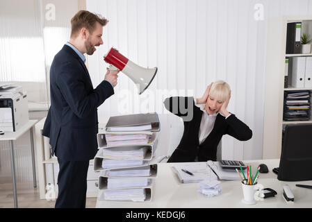 Boss Shouting At Young Businesswoman Through Loudspeaker In Office Stock Photo