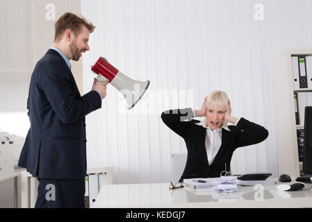 Boss Shouting At Young Businesswoman Through Loudspeaker In Office Stock Photo