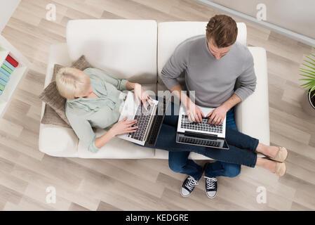 High Angle View Of Young Couple Relaxing On Sofa Using Laptop Stock Photo
