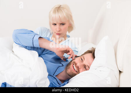 Woman Looking At Man Talking On Mobile Phone In Bedroom Stock Photo