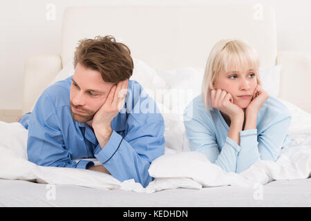 Sad Couple Lying In Bed Ignoring Each Other In Bedroom At Home Stock Photo