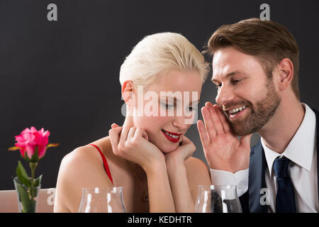 Portrait Of Young Man Whispering In Woman's Ear At A Restaurant Stock Photo