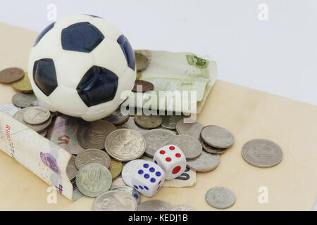 Mini soccer ball on top of playing cards with dices and money in different currency. Concept of betting and gambling. Stock Photo