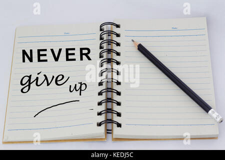 Motivational words NEVER GIVE UP written on one page of an opened notebook with pencil beside it. Stock Photo