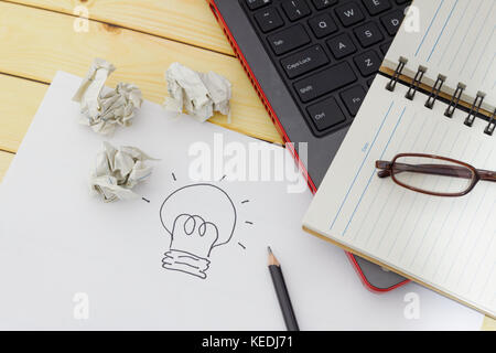 Idea,creativity and innovation concept. Spectacles, blank notebook, pencil, laptop, crumpled papers and a piece of white paper with a light bulb drawi Stock Photo