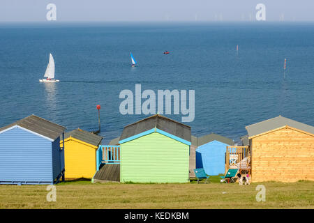 Colourful beach hits at the bottom of the grass area  in Tankerton, known as the slopes. The windfarm can be seen on the horizon Stock Photo