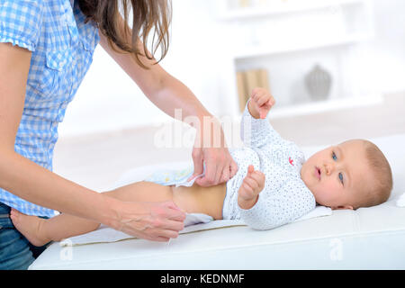 mom puts on diaper baby changing table Stock Photo