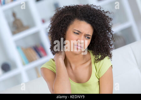 young woman sitting on the bed with pain in neck Stock Photo