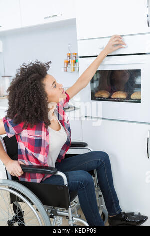 disabled woman baking bread roll in kitchen oven Stock Photo