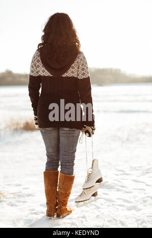 Woman carrying ice skates standing at the edge of a frozen lake Stock Photo