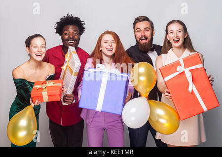 Beautiful and happiness friends celebrating new year. Showing at camera many gift box and toothy smiling. Indoor shot on gray background Stock Photo