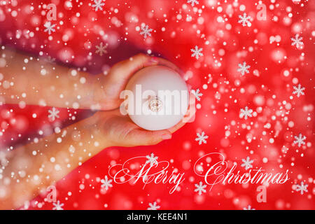 Merry Christmas background or gift card - child's hands holding white ornament on red background Stock Photo