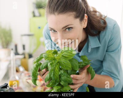 Smiling woman smelling fresh basil at home and preparing healthy food in the kitchen Stock Photo