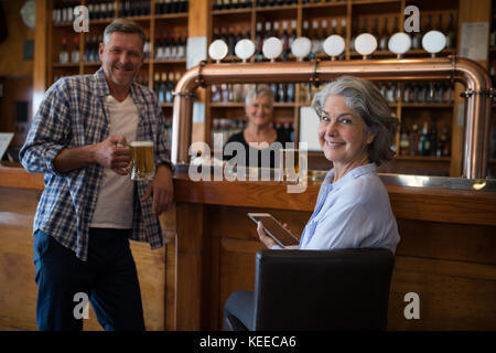 Portrait of happy man having beer and woman using digital tablet at counter in bar Stock Photo