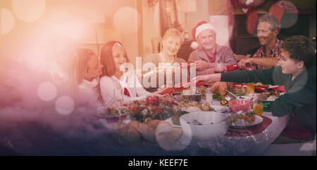 Clouds covering snowcapped mountains against sky against smiling family pulling christmas crackers at the dinner table Stock Photo