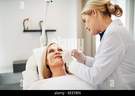 Young female doctor focused on performing a botox injection to the cheek of a mature woman lying on a table in a beauty clinic Stock Photo
