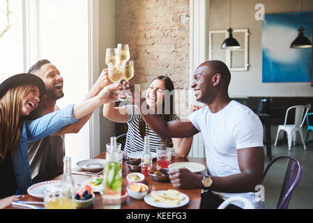 Four young friends at dinner reunion at restaurant clinking glasses with wine and laughing. Stock Photo