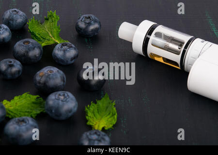 white electronic cigarette on a dark table, next to a scattered berry Stock Photo