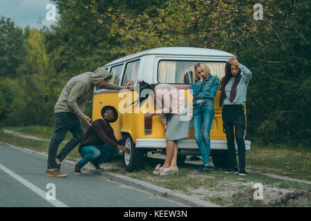 multiethnic friends standing near broken minivan on road Stock Photo