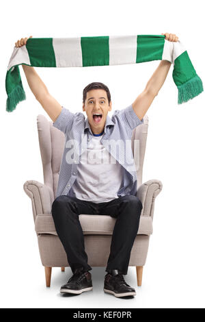 Excited sports fan sitting in an armchair and holding a scarf isolated on white background Stock Photo