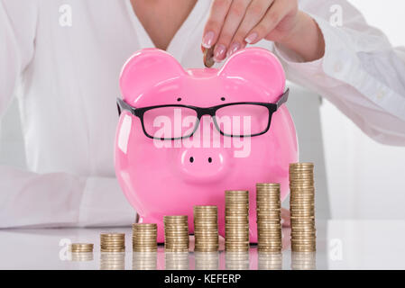 Close-up Of A Female's Hand Inserting Coin In Piggybank Stock Photo