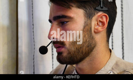 Young male home worker talking with customer or client through headset and microphone, working from his living room in front of computer late at night Stock Photo