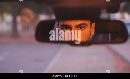 Serious young man driving car and looking at camera through back mirror Stock Photo