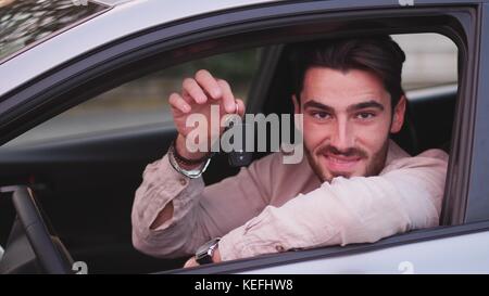Handsome young man holding bunch of keys, looking in camera, sitting in his new car Stock Photo