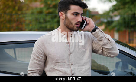 Handsome Young Man talking on mobile phone while leaning on a car Stock Photo