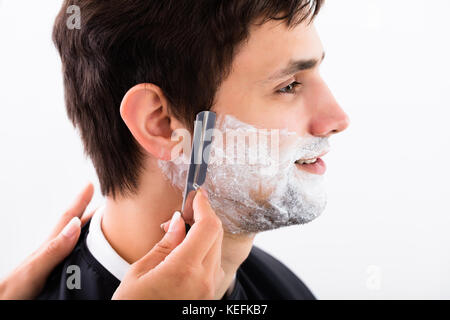 Close-up Of A Hairdresser Shaving Man's Beard By Applying Shaving Cream Stock Photo