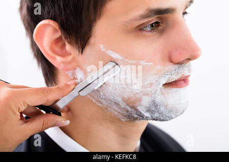 Close-up Of A Hairdresser Shaving Man's Beard By Applying Shaving Cream Stock Photo