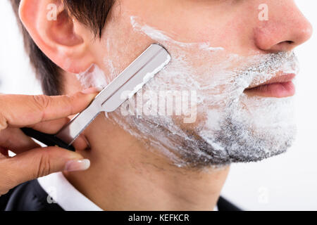 Close-up Of A Hairdresser Shaving Man's Beard By Applying Shaving Cream Stock Photo