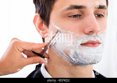 Close-up Of A Hairdresser Shaving Man's Beard By Applying Shaving Cream Stock Photo