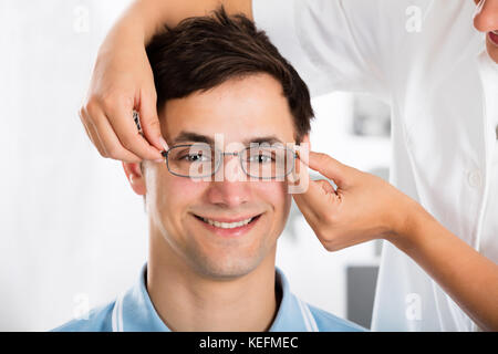 Close-up Of An Optician Helping Young Male Patient With New Eyeglasses Stock Photo