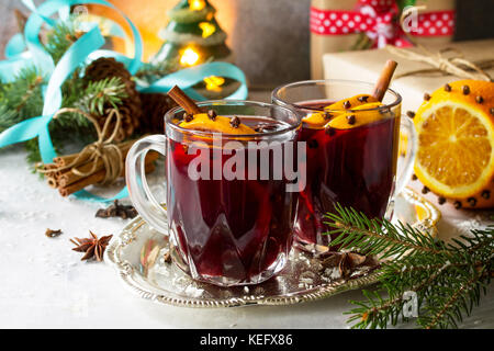Homemade Christmas cocktail mulled wine red wine with cinnamon sticks, oranges and cloves, served in two cups on a gray stone or slate. Copy space. Stock Photo