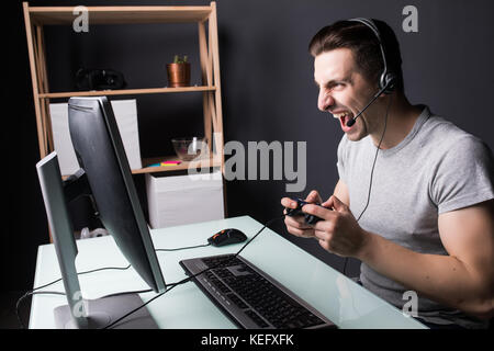 technology, gaming, entertainment, let's play and people concept - angry screaming young man in headset with pc computer playing game at home and stre Stock Photo