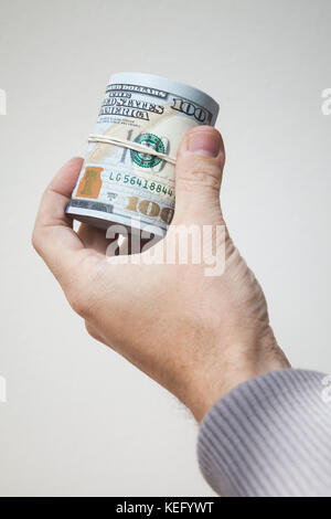 Roll of new One Hundred Dollars notes in male hand over gray wall Stock Photo