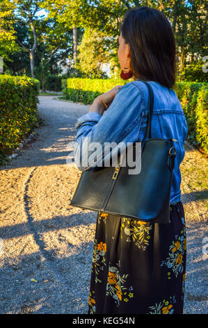 A young woman in a park, casually dressed, holding a black handbag Stock Photo