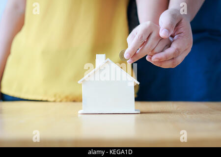 Close up shot hands of man and woman putting the coin to house piggy bank ratio metaphor and concept for Couple saving money for buy home and real est Stock Photo