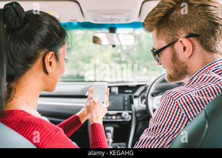 Multiethnic lover couple, white man and black Asian girl using navigator system app on smart phone in car. Modern gadget lifestyle, family travel Stock Photo