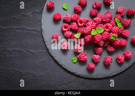 Ripe raspberries on slate dish on black background. Stock Photo