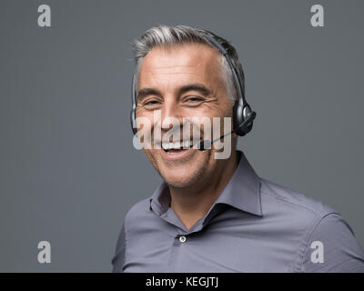 Cheerful customer support phone operator with headset, he is talking with a customer and smiling Stock Photo