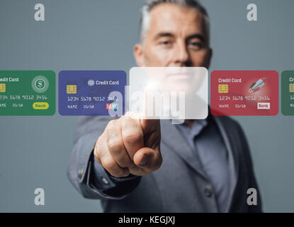 Businessman selecting a credit card on a visual interactive interface and choosing a payment method, he is touching a blank card; online banking and p Stock Photo