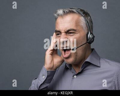Angry aggressive customer support phone operator with headset, he is yelling and having a dicussion with a customer Stock Photo