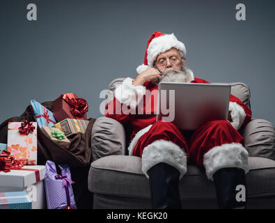 Santa Claus relaxing at home and connecting with a laptop, he is chatting and social networking, Christmas time and technology concept Stock Photo