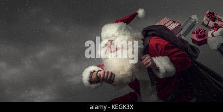 Santa Claus running and delivering Christmas presents: he is late and losing gifts from his sack Stock Photo