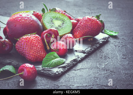 Mix of Juicy summer fruits and berries. Strawberry, cherry, kiwi and peaches on black slate plate. Toned Stock Photo