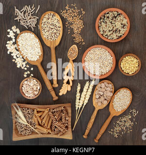 High fiber health food of whole wheat pasta, cereal and grains in bowls and spoons on rustic oak background. Stock Photo