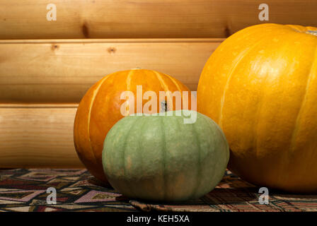 three different-colored pumpkins of different sizes on a table on a background of a log wall close-up Stock Photo